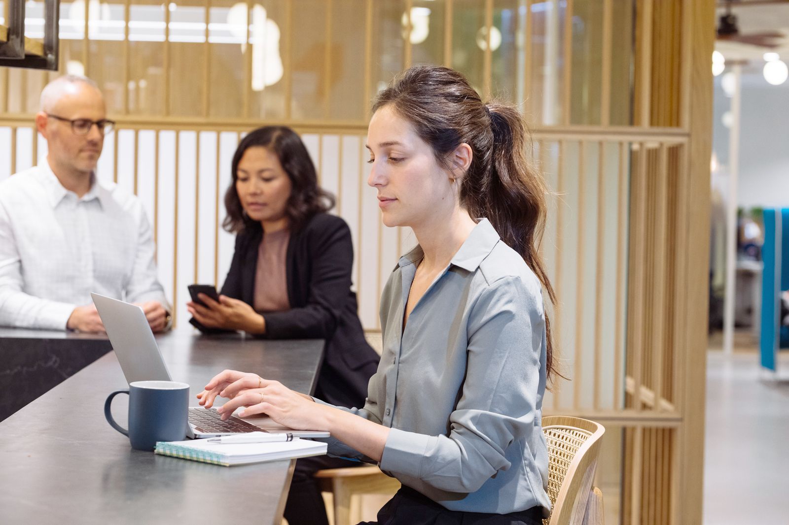 Three colleagues working on laptops and a phone at a shared desk