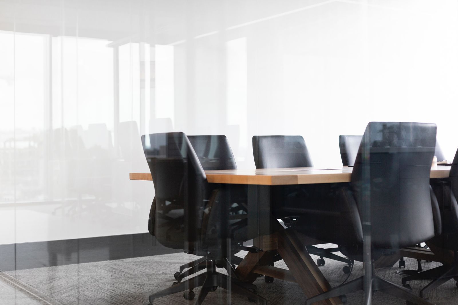 Bright, empty glass-walled meeting room with a long table and black chairs