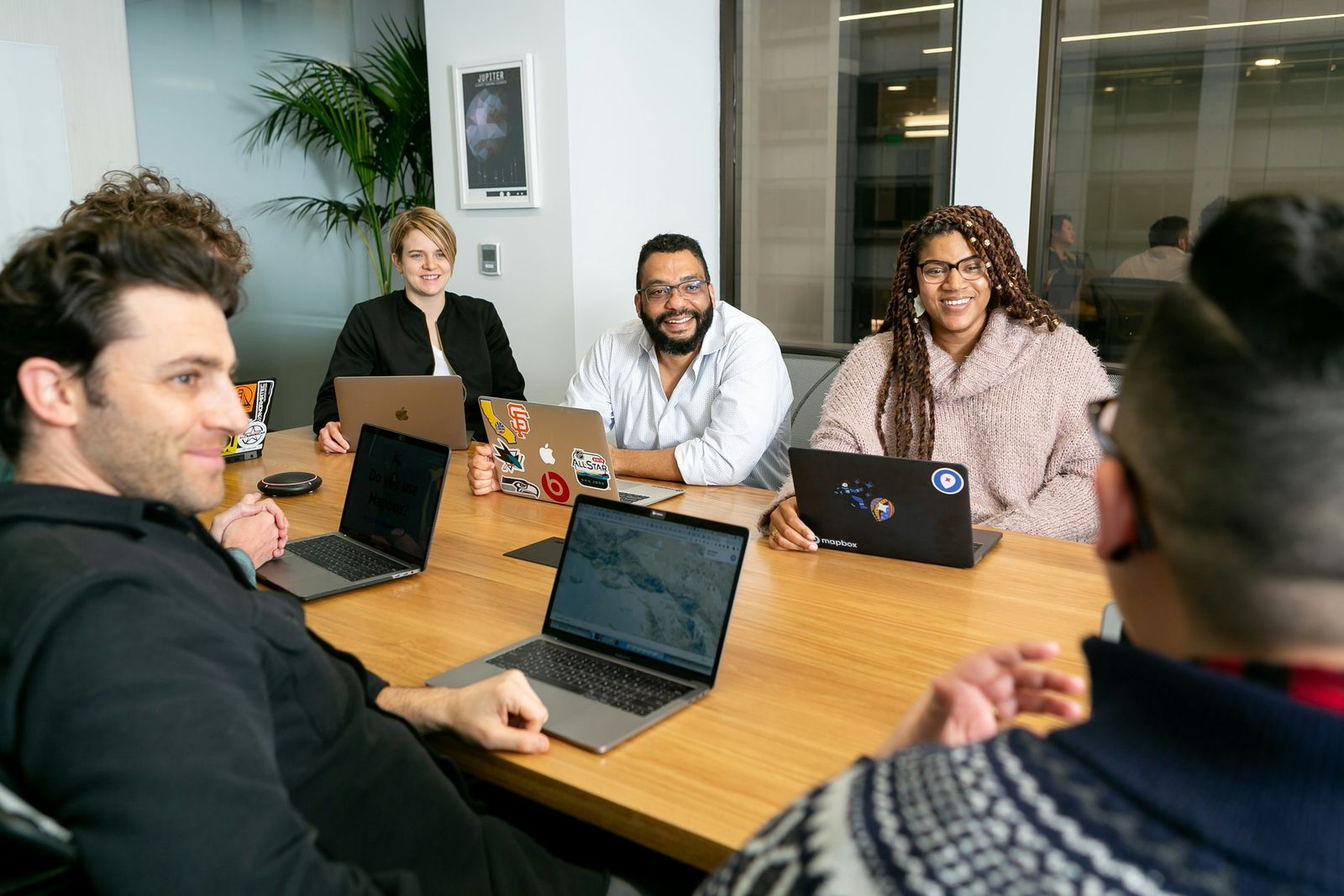 Colleagues with laptops around a table in a bright office, listening to a teammate