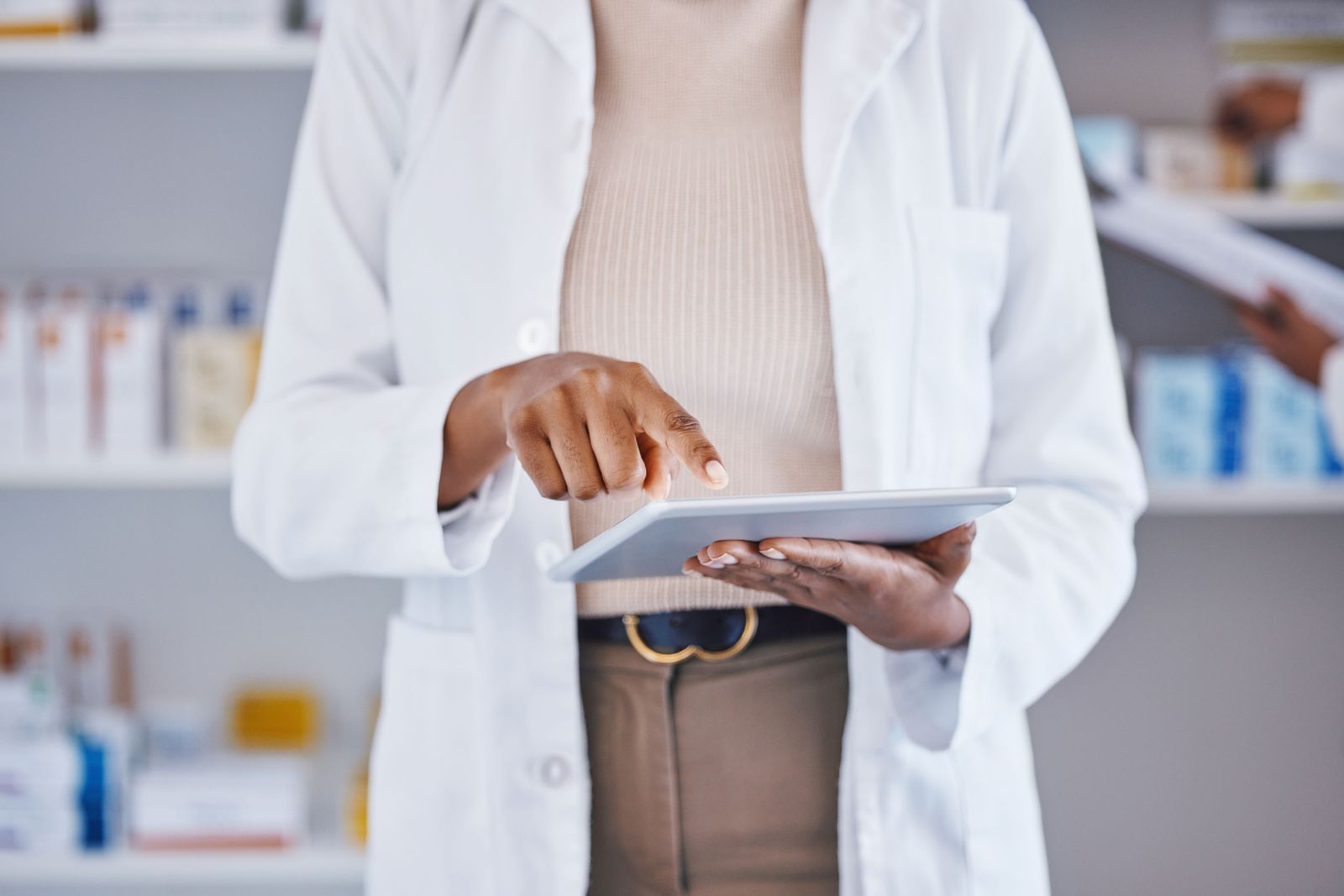 Clinician in a white coat using a tablet in a pharmacy