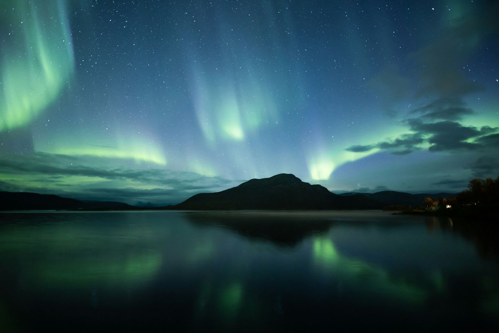 Northern lights over a still Nordic lake and hills at night