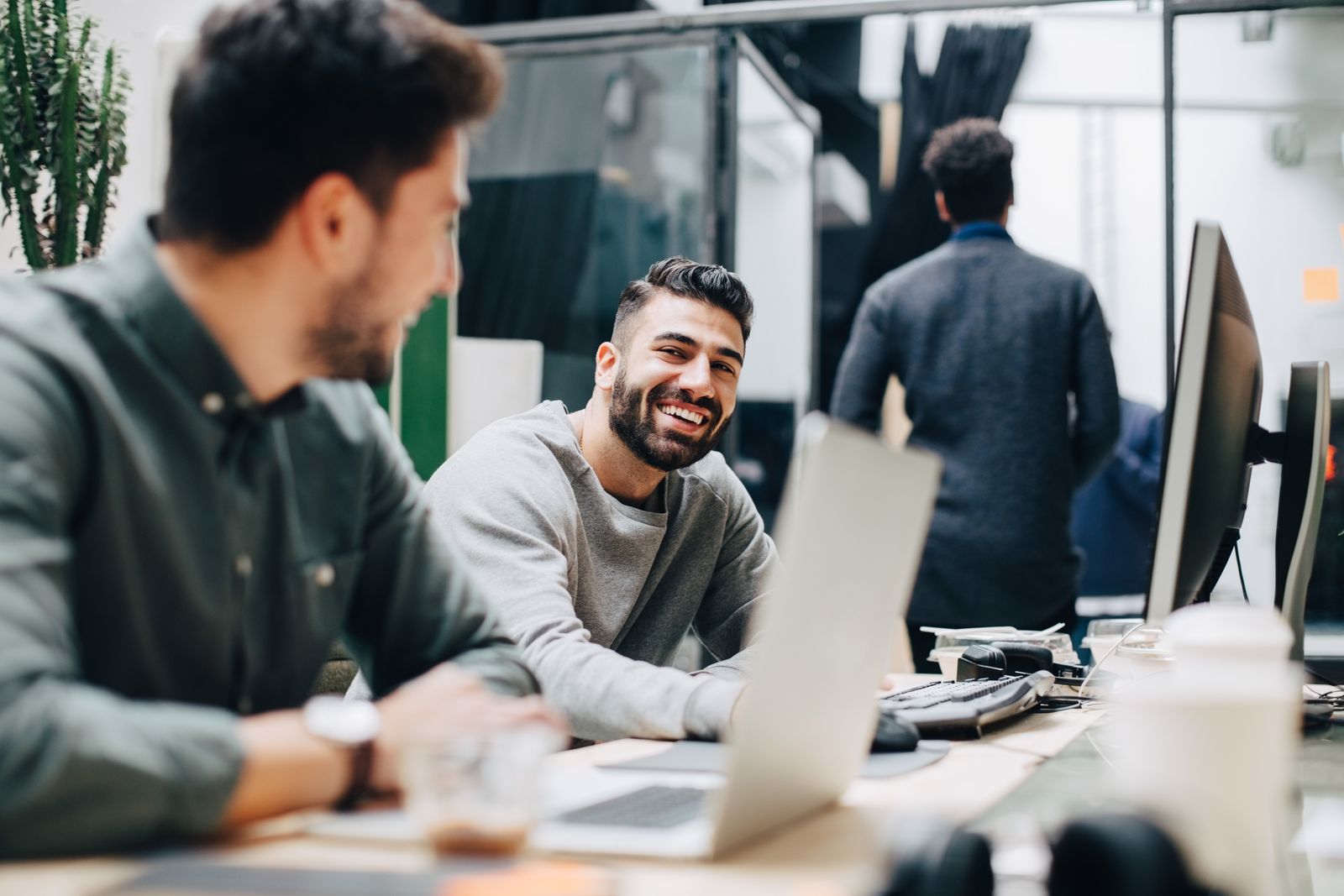Two young colleagues laughing together at their laptops in an open-plan office